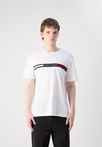 Valge puuvillane T-särk lühikeste varrukatega, millel on mustade ja punaste triipudega graafika rinnal ning keskel "TOMMY HILFIGER" logo.