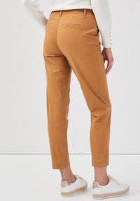 Pantalons beige à coupe slim, en coton, avec une texture lisse et deux poches arrière, associés à des chaussures blanches et un pull léger.
