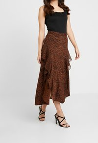 Haut sans manches noir avec un col à volants associé à une jupe maxi imprimé léopard orange dotée d'un design superposé et d'une fente sur le côté.