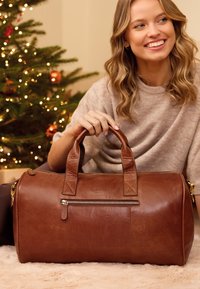 Pruun nahast spordikott ümara kujuga, tugeva käepidemega, esiküljel tõmblukuga tasku ja diskreetse brändinguga. Pehme tekstuur, minimalistlik disain.