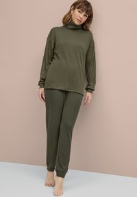 Olijfgroen loungeoutfit bestaande uit een lange mouwen turtleneck en tapered joggerbroek, beide in een zachte, gestructureerde stof.