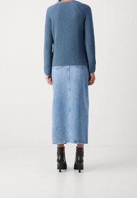 Pull en tricot bleu avec manches raglan, accompagné d'une longue jupe en jean bleu clair. Bottes noires à talons complètent la tenue.