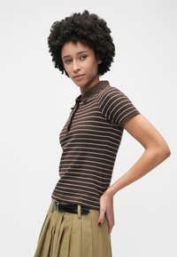 Polo rayé marron à manches courtes avec un col, associé à une jupe plissée kaki. Texture douce en coton.