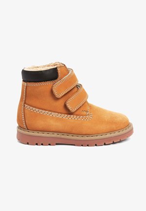 Tanfarbene Wildleder-Ankle Boots mit zwei verstellbaren Klettverschlüssen, weichem Innenfutter, brauner Gummisohle und kontrastierenden Nähdetails.