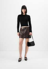 Top corto nero a maniche lunghe, mini gonna in pelle marrone con zip frontale e due tasche, borsa nera e scarpe con tacco nere.