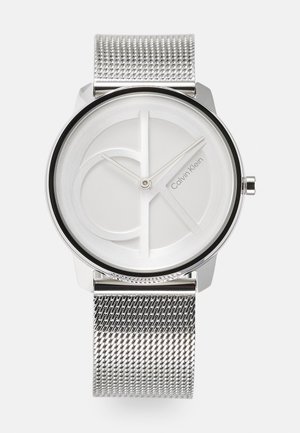 Montre à bracelet en mailles argentées de Calvin Klein, avec un cadran blanc minimaliste portant une marque discrète et une lunette noire élégante. Forme ronde.