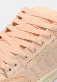 Light pink sneaker with textured leather, thick laces, and a rubber sole. Features "GLOBE" logo in gold on the side.