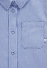 Cămașă din catifea ușor albastră, cu închidere cu nasturi în față, guler ascuțit, un singur buzunar pe piept și un logo mic în formă de inimă pe buzunar.