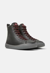Hoge sneakers van donkergrijs leer met bruine veters en een grijze zool, voorzien van een Camper-logo op de tong. Geschikt voor casual gebruik.