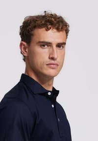 Marineblauw poloshirt met een kraag, voorzien van een knoopsluiting met twee knopen en een kleine witte accent. Glad materiaal met een getailleerd ontwerp.