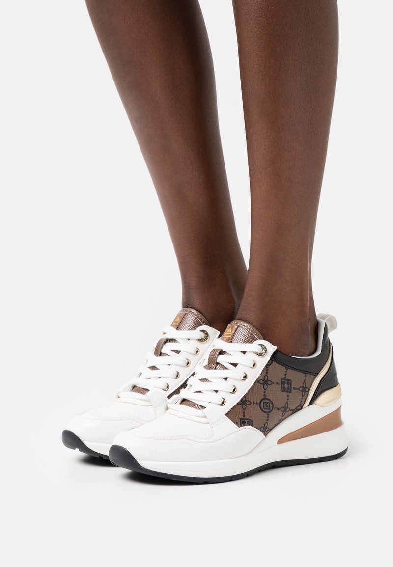 Vita och bruna sneakers med ett mönstrat sidopanel, snören, metalliska detaljer och en kraftig klack. Har en gummisula för bra grepp.