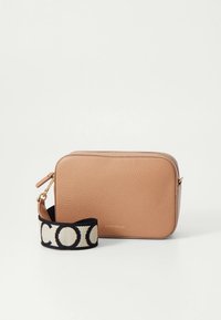 Tan-färgad crossbody-väska i läder med en texturerad yta, dragkedja som stängning och ett avtagbart svart band med ett kontrasterande logomönster.
