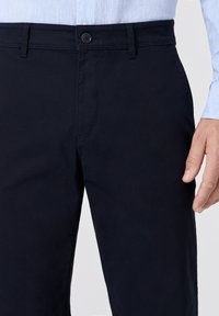 Pantaloni blu navy realizzati in tessuto misto cotone, caratterizzati da una superficie liscia, chiusura con bottone standard e zip, e tasche frontali.