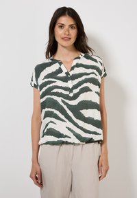 Blusa de manga corta en patrón de cebra verde y blanco, con un cuello tipo notch y un corte relajado, hecha de una tela ligera.