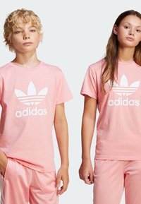 Pink cotton t-shirts featuring a large white Adidas logo and three stripes design on the sleeves, paired with matching pink shorts.