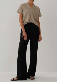 Béžový texturovaný top s výstřihem do V a krátkými rukávy, doplněný černými kalhotami s vysokým pasem a širokými nohavicemi a černými plochými sandály.