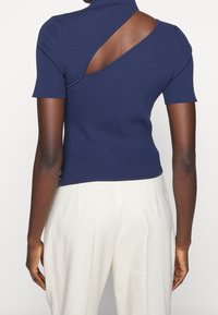 Marinblå ribbad stickad topp med korta ärmar, med en asymmetrisk utskärning på baksidan och en hög krage. Skräddarsydd passform, slät textur.