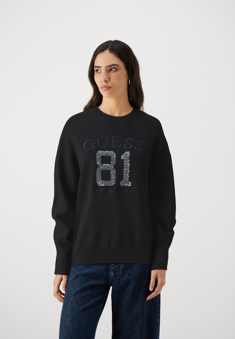 Svart sweatshirt med rund halsringning, med blå "GUESS" text och en paljettdekorering av "81" på framsidan. Långa ärmar och avslappnad passform.