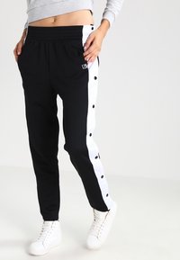 Zwarte sportbroek met witte zijpanelen en drukknopen. Gemaakt van zachte stof met een elastische tailleband. Eenvoudig logo-detail op de voorkant.