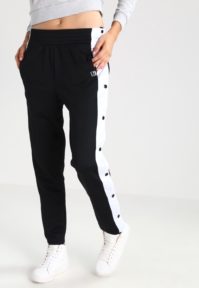 Zwarte sportbroek met witte zijpanelen en drukknopen. Gemaakt van zachte stof met een elastische tailleband. Eenvoudig logo-detail op de voorkant.