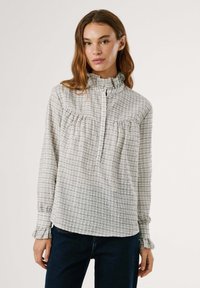 Sivino in belo karirano srajco z naborkom okoli ovratu, z gumbi in nabranim detajlom na prsih. Dolgi rokavi z naborki na koncu.