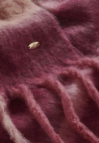 Lyserød og mauve struktureret strikstof med et bølget mønster og et metalisk ovalt mærke med et design, der fremhæver blødhed og lag-på-lag.