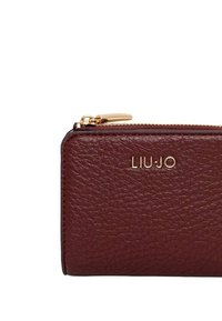 Portafoglio in pelle bordeaux con superficie testurizzata, cerniera in metallo dorato e logo impresso a rilievo. Forma rettangolare compatta.