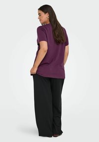 Kort lilla t-shirt med korte ærmer, kombineret med løstsiddende sorte bukser. Glat stof med en afslappet pasform og afrundet kant.