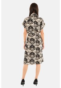 Vestido con estampado en blanco y negro, de mangas cortas, cintura ceñida con cinturón, con falda a la altura de la rodilla y textura suave. Llevado con tacones altos negros.