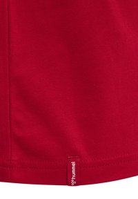 Rød T-shirt lavet af glat bomuldsstof, med et lille mærke med brandnavnet "hummel" ved den nederste kant. Ensfarvet design.