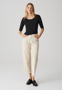 Schwarzes T-Shirt mit kurzen Ärmeln, kombiniert mit cremefarbenen, weiten Hosen mit hoher Taille und rohem Saum. Schwarze Loafer runden das Outfit ab.