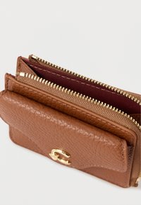 Portefeuille en cuir marron avec ferrures dorées. Double compartiment zippé révélant un intérieur bordeaux. Surface texturée avec détails de couture visibles.