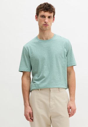 Light green striped t-shirt with short sleeves and a round neckline, made of soft material, paired with beige trousers.