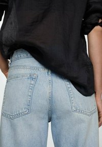 Jeans de mezclilla azul claro con una cintura alta, pierna acampanada y dos bolsillos traseros. La tela tiene una textura suave y un acabado desgastado.