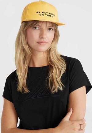 Gele pet met zwarte tekst "WE GET HIGH ON TIDES." Zacht materiaal, gestructureerd ontwerp, gebogen rand, gedragen met een zwart T-shirt.