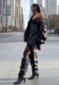 Čierne čipkované šaty s lemom s strapcami, v kombinácii s nadrozmernou čiernou koženou bundou. Celý vzhľad dopĺňajú elegantné čierne čižmy s podpätkom po kolená.