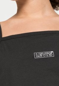 Černý tílko vyrobené z bavlny, s čtvercovým výstřihem a bílým logem Levi's na oblasti hrudníku. Hladká textura s úzkými ramínky.