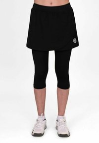 Falda corta deportiva negra superpuesta sobre leggings capri negros, con cinturilla elástica y un detalle de logotipo en el lateral. Tejido ligero.