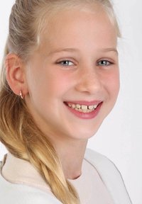 Glunderend kind met lang, lichtblond haar. Draagt kleine, ronde oorbellen. Lichte huid met sproetjes, tegen een eenvoudige witte achtergrond.