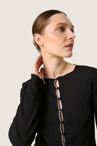 Must mustriga ülemine osa, mis on varrukatega, skaalopitud kaeluse ja nööbidetailiga, millel on kontrastsed valged aktsendid esiäärisel.