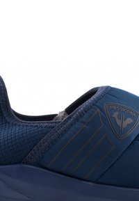 Námořnické sportovní boty s texturovaným síťovaným svrškem, elegantním designem, gumovou podrážkou a reliéfním logem. Obsahují švy a tmavé horizontální pruhy.