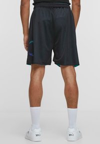 Svart treningsshorts med mesh-struktur, elastisk midjebånd og turkise detaljer i kanten. Har et geometrisk mønster på siden.