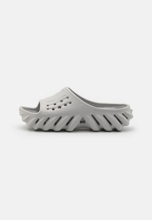 Lichtgrijze instapklomp met ventilatiegaten bovenop en een uniek geribbelde, open zool voor ademend vermogen en comfort.