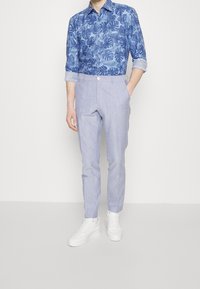 Knappad blå skjorta med bladmönster, i kombination med ljusblå skräddarsydda byxor och vita sneakers. Slät textur, snygg passform.