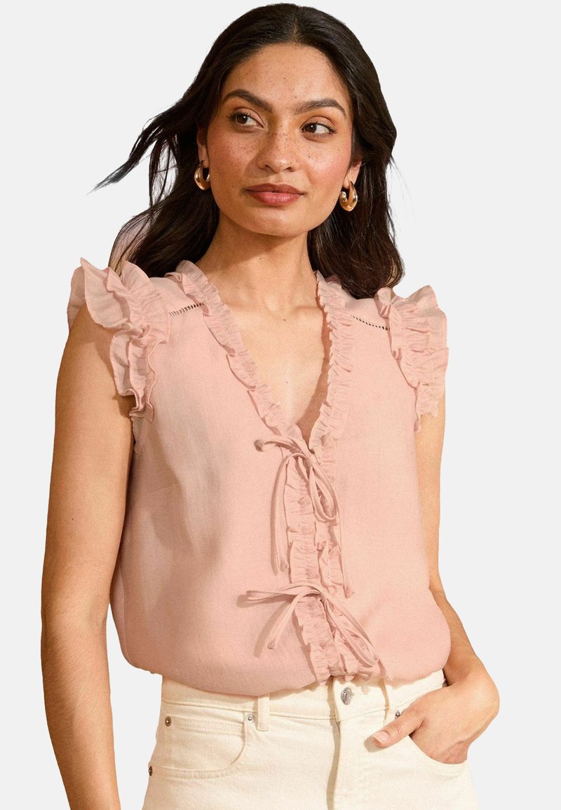 Blusa senza maniche di un delicato rosa chiaro con scollo arricciato e laccio centrale. Tessuto morbido, vestibilità comoda e cuciture dettagliate lungo i ruffles.