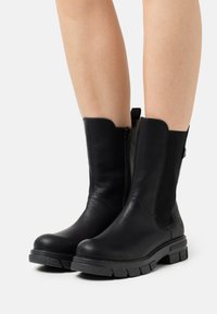 Bottines en cuir noir avec des panneaux latéraux élastiques, un bout arrondi et des semelles en caoutchouc texturé. Comprend une fermeture éclair sur le côté pour un enfilage facile.