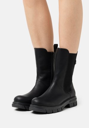 Bottines en cuir noir avec des panneaux latéraux élastiques, un bout arrondi et des semelles en caoutchouc texturé. Comprend une fermeture éclair sur le côté pour un enfilage facile.