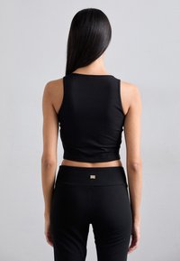 Črn skrajšan tank top izdelan iz gladkega blaga, z okroglo ovratnico in prilegajočim dizajnom. Pairswith visoko pasnimi črnimi leginami.