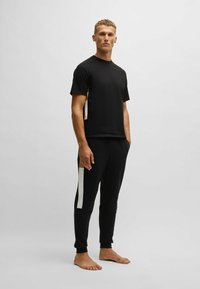 Black athletic shirt with short sleeves and a contrasting beige and white side panel, paired with matching black tapered pants featuring side striping.