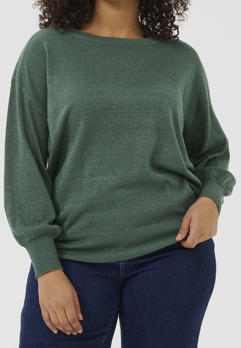 Groene, metallic gebreide sweater met een losse pasvorm, brede bootcollar en lange mouwen. Bevat ribgebreide boorden en een zoom, gecombineerd met donkere jeans.